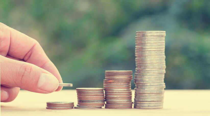 Assurance vie : une main qui ajoute des pièces progressivement sur des tas de pièces de monnaie